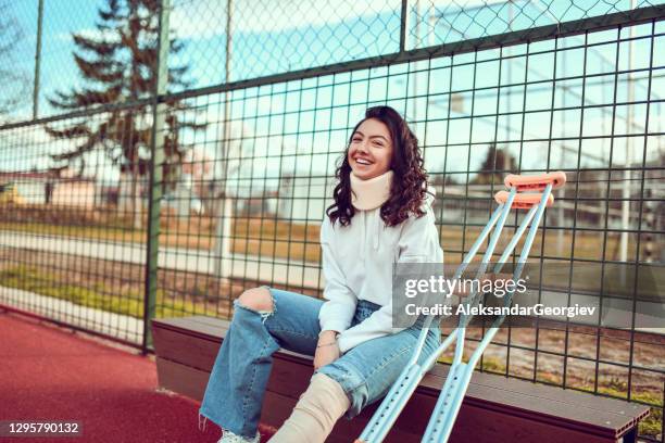 smiling female with crutches and neck brace sitting on bench - woman cervical collar stock pictures, royalty-free photos & images