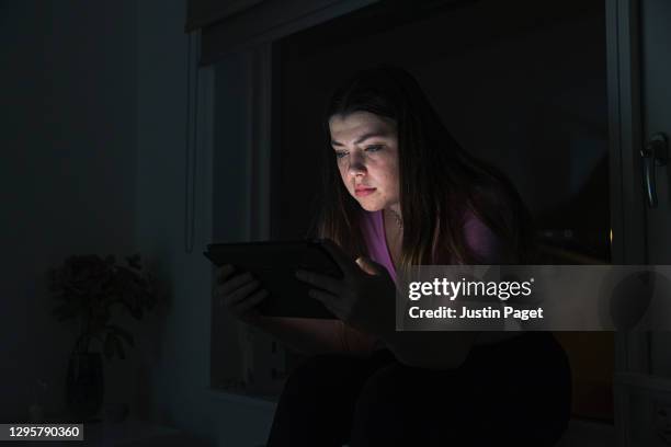 sad teenage girl using digital tablet at night - child mental health wellness stock-fotos und bilder