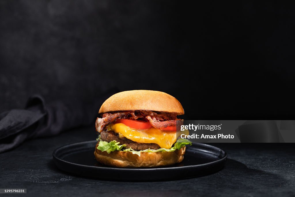 Hamburger di formaggio con pancetta su sfondo nero scuro