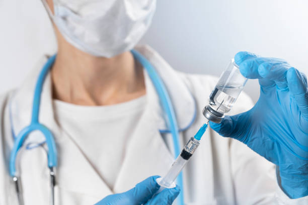 um médico de jaleco branco, máscara médica e luvas de proteção pega o medicamento de uma ampola de vidro e coloca em uma seringa. a vacina está nas mãos de uma enfermeira. o conceito de tratamento e prevenção da propagação da infecção por covid-19, vírus e pneumonia. - fotos de stock de médico dando injeção, fotos e imagens livres de direitos autorais