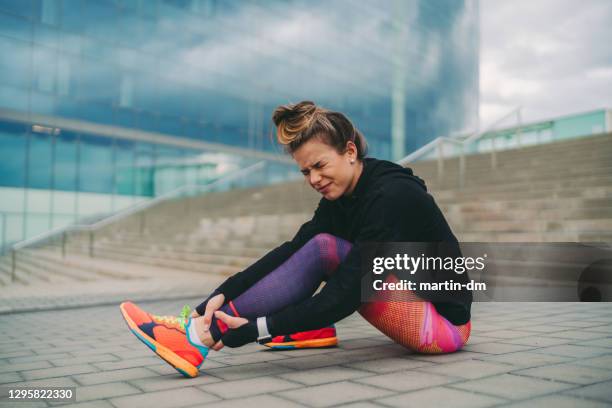 sportswoman with sprained ankle sitting on ground - twisted ankle stock pictures, royalty-free photos & images