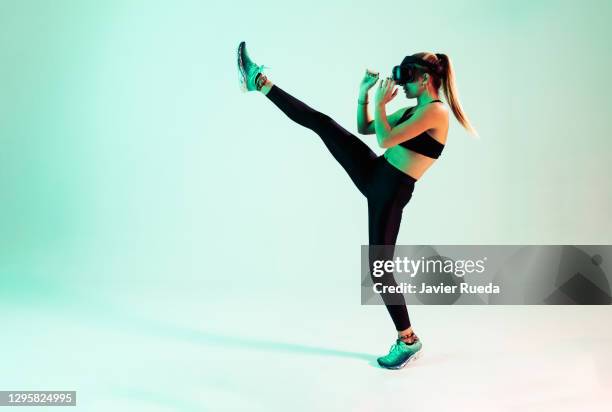 studio portrait of young fitness girl with sporty body and vr glasses, playing video games with virtual reality headset, doing kick boxing training in studio with bright background. beautiful fit woman. augmented reality, future technology concept. vr - kickboxing equipment stock pictures, royalty-free photos & images