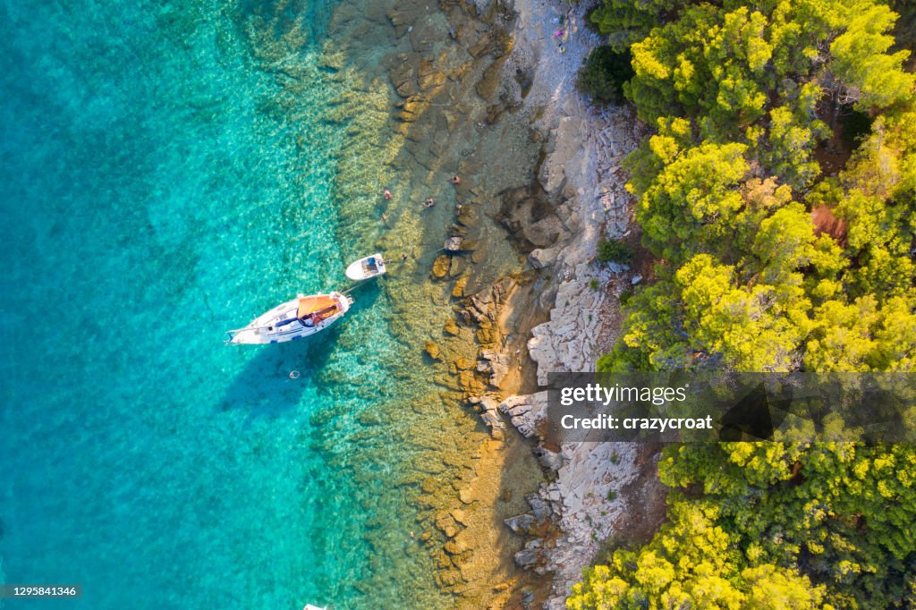 Bateau à voile à l’ancre à côté du rivage rocheux avec une forêt de pin à l’arrière-plan