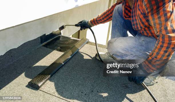 roofer preparing part of bitumen roofing felt roll for melting by gas heater torch flame - membrana fotografías e imágenes de stock