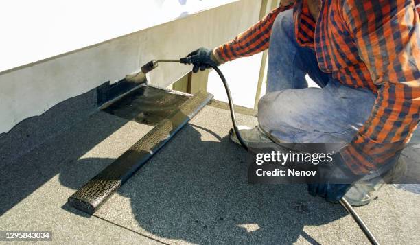 roofer preparing part of bitumen roofing felt roll for melting by gas heater torch flame - waterproofing stock pictures, royalty-free photos & images