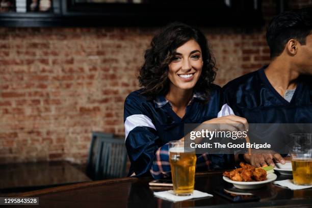 portrait of mid adult woman eating and drinking in sports bar - asa de frango imagens e fotografias de stock