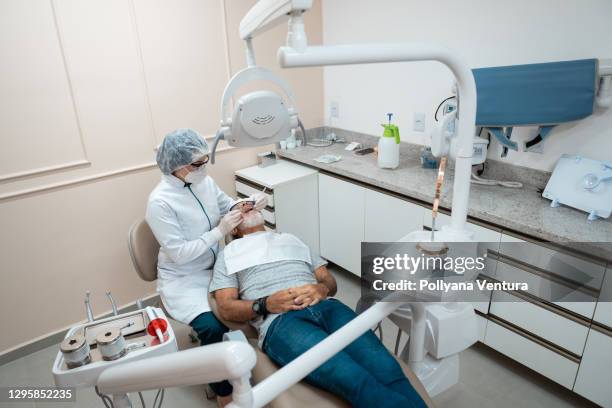 dentist examining the teeth of senior man - general view stock pictures, royalty-free photos & images