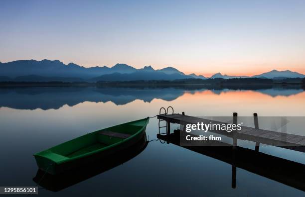 lake with jetty and boat in the alp mountains (allgäu/ bavaria/ germany) - blaue stunde stock-fotos und bilder