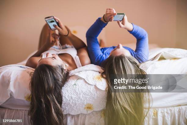 teenage girls lying on bed looking at smart phones - インスタグラム ストックフォトと画像