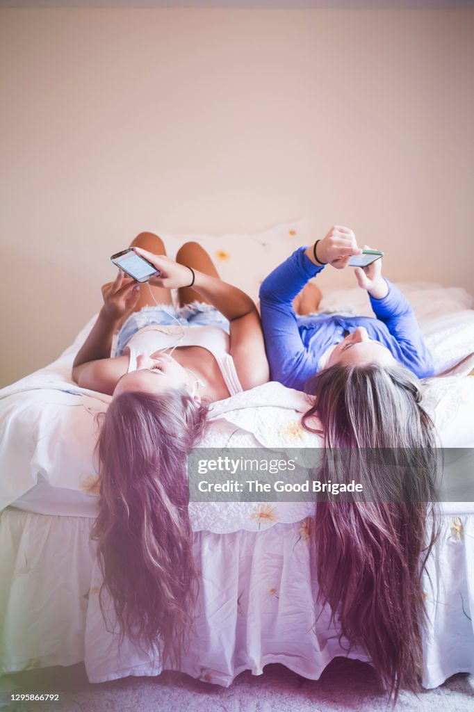 Teenage girls lying on bed checking smart phones