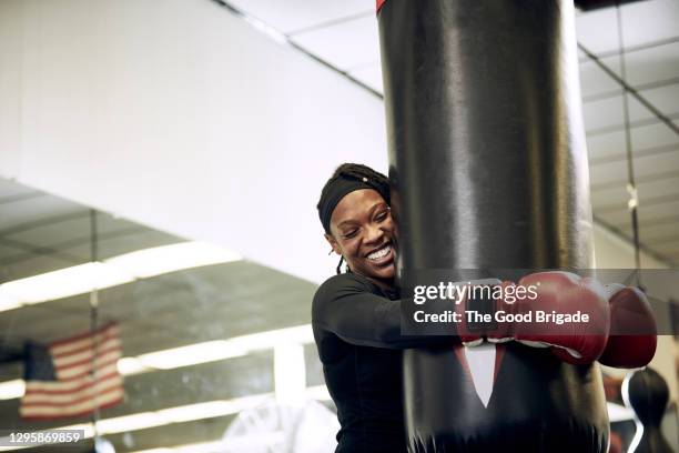 happy female boxer holding punching bag at health club - 女子ボクシング ストックフォトと画像