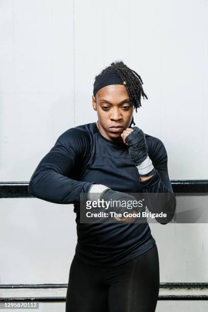 determined female boxer standing in fighting stance against white wall at gym - boxing womens stock pictures, royalty-free photos & images