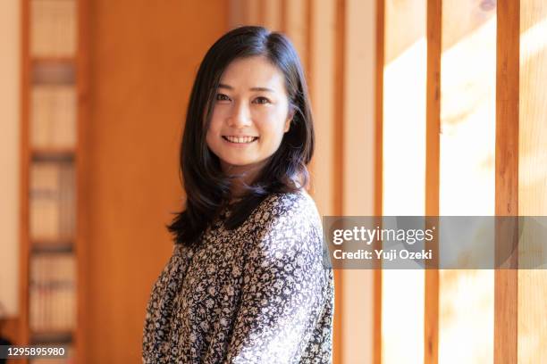 asian young adult woman smiling by the window of a woody cafe - 会社員 笑顔 日本人 ストックフォトと画像