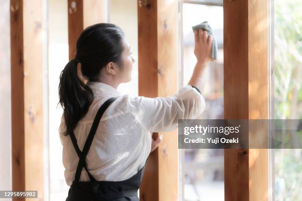 asian young woman wiping the window glass of a cafe restaurant wearing an apron with a ponytail - きれいにする ストックフォトと�画像