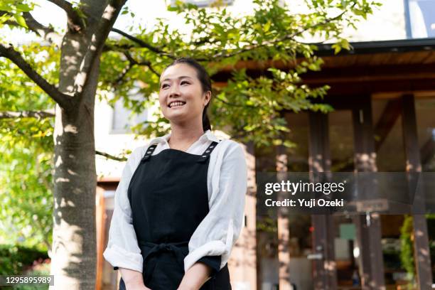 asian young adult woman smiling in front of a woody cafe, is also the owner of this cafe restaurant. - reopening ストックフォトと画像