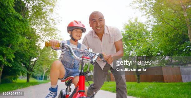 father helping daughter to ride bicycle - indian family in their 40's with kids imagens e fotografias de stock