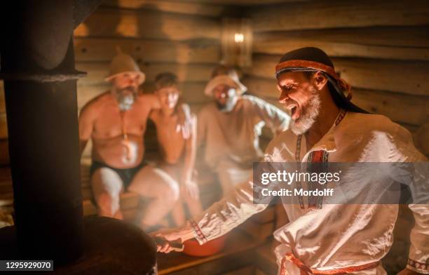 bath attendant is throwing ladle with water in sauna stove to generate steam. russian customs and traditions - young boy in sauna stock pictures, royalty-free photos & images