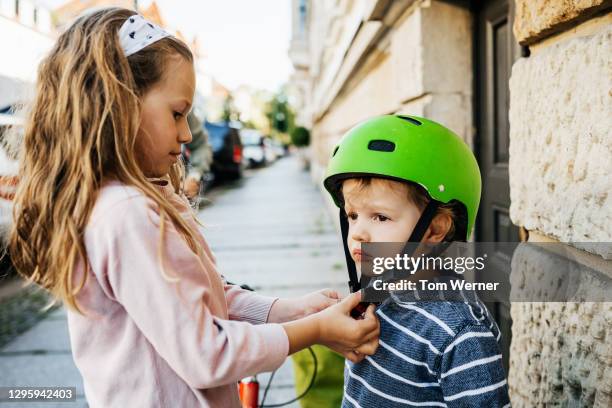 young girl helping younger brother fit his bike helmet - sisters stock-fotos und bilder