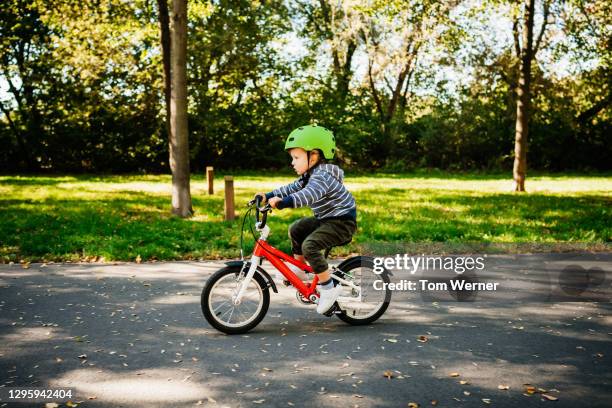 young boy riding new red bike in park - cycling helmet stock pictures, royalty-free photos & images