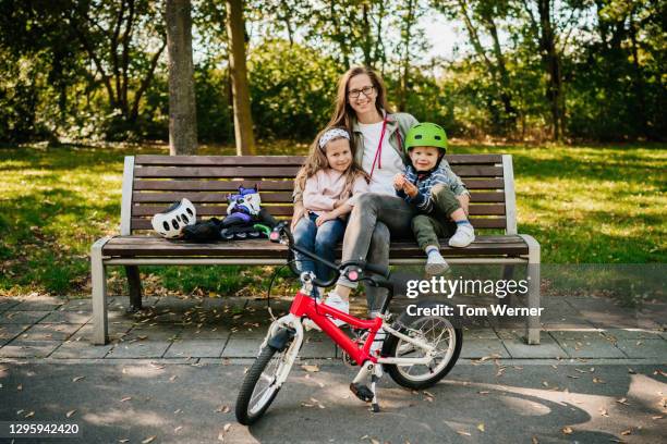 portrait of mother sitting with two children on park bench - fahrrad grün stock-fotos und bilder