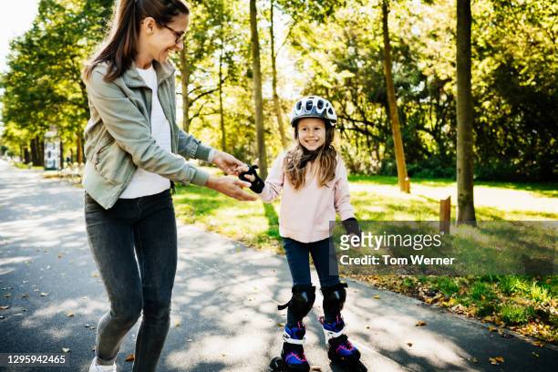 mom helping young daughter while learning to roller blade - patín en línea fotografías e imágenes de stock