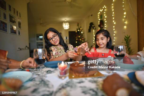 girls enjoying plum cake with dinner together with family on christmas eve in a house decorated with christmas tree and string lights - christmas cake stock pictures, royalty-free photos & images