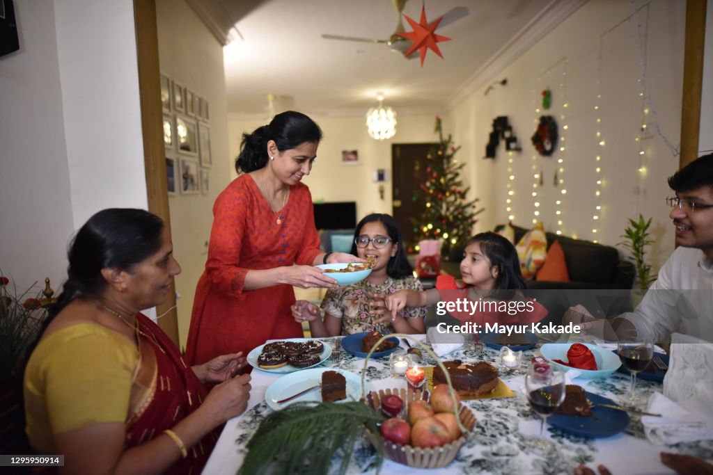Woman serving donuts to family and family enjoying dinner together on a dining table on Christmas Eve