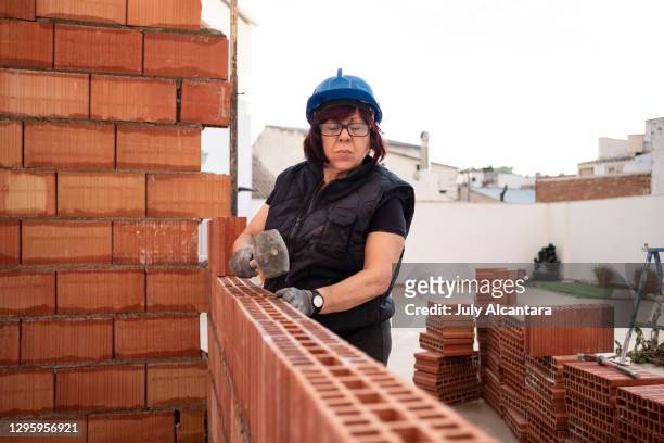 mature woman bricklayer lays bricks in the construction and remodeling of the terrace room of a house - mason bricklayer stock pictures, royalty-free photos & images