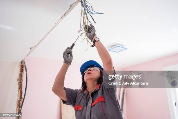 mature woman bricklayer adjusts the electric and telephone line in the remodeling of the room of a house - female bricklayer stock pictures, royalty-free photos & images