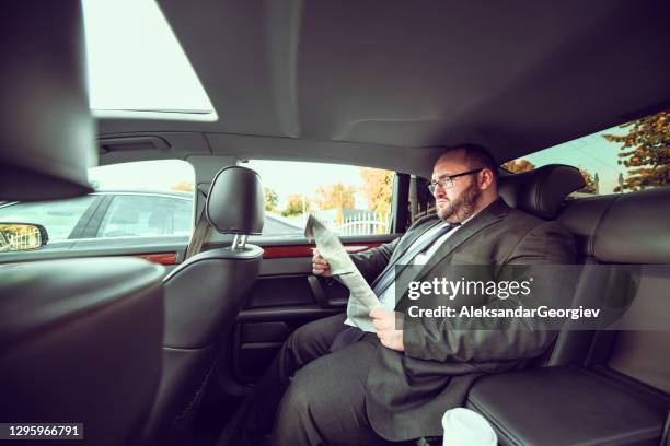 overweight businessman reading newspaper in back of car - man in car reading newspaper stock pictures, royalty-free photos & images
