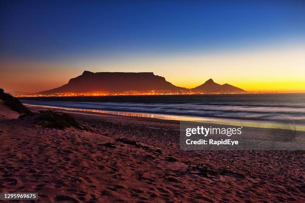 espectacular vista crepuscular de table mountain, ciudad del cabo, sudáfrica a través de table bay con la ciudad ardiendo de luz - table mountain south africa fotografías e imágenes de stock