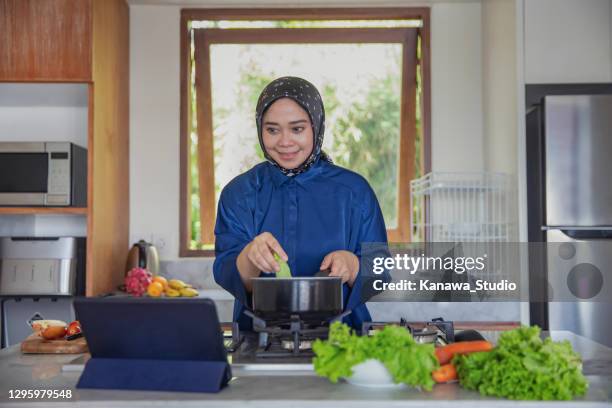 attraktive muslimische frau nach kochanweisungen aus video auf digitalem tablet. - muslims prepare for eid in indonesia stock-fotos und bilder