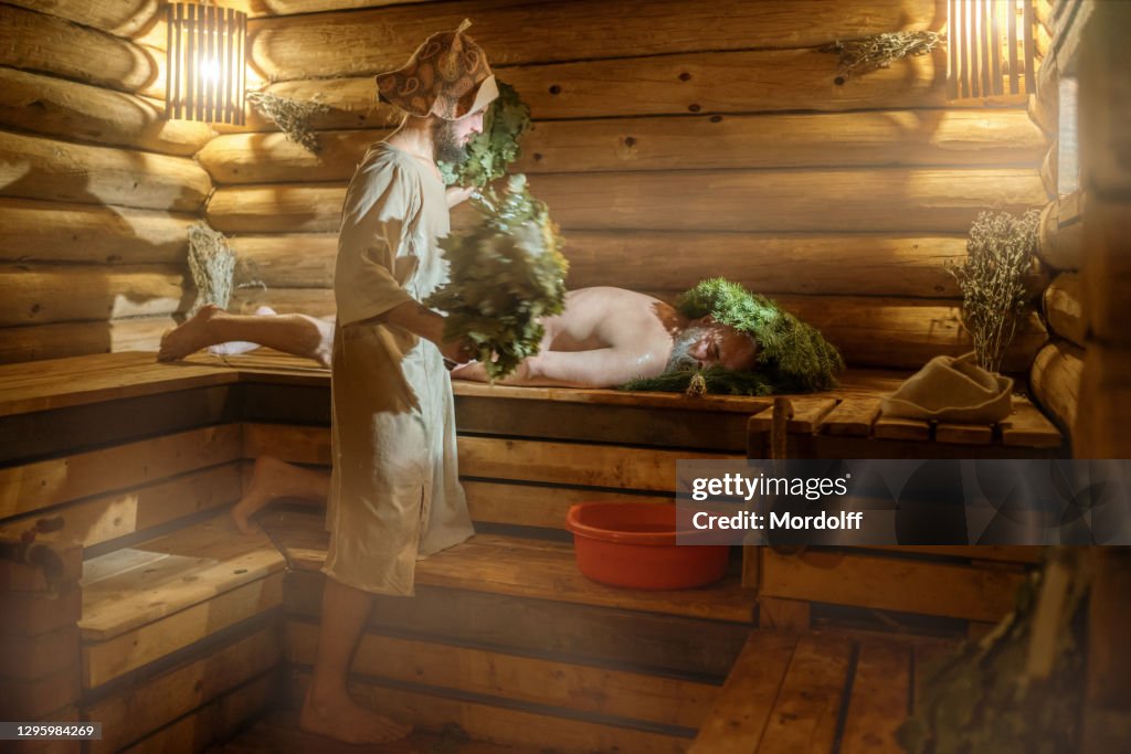 O homem está relaxando na sauna russa. Atendente de banho está servindo-o