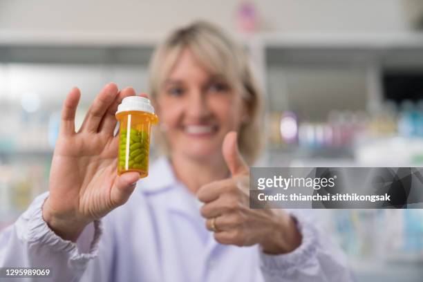 close up smile medical pharmacist woman holding pill bottle and thumbs up in pharmacy. - friends smile stock-fotos und bilder