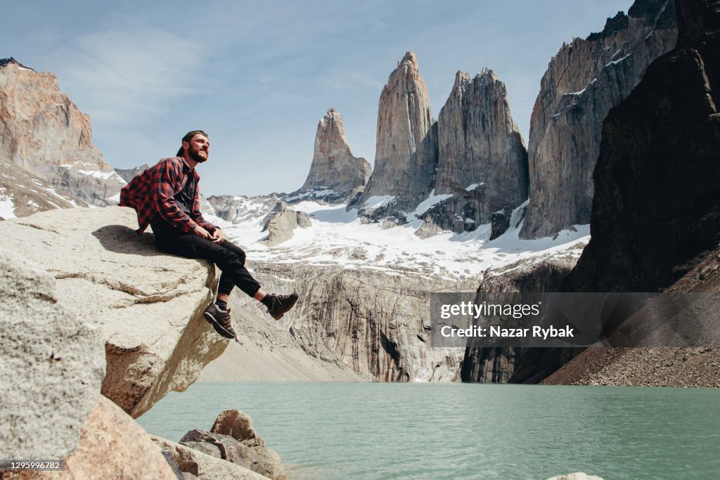 El hombre está sentado en la vista panorámica del fondo del Parque Nacional Torres del Paine