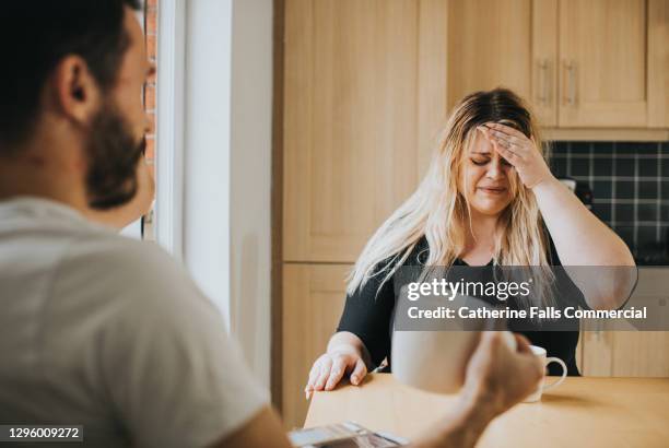 distressed woman at a kitchen table talking to her partner - fight fotografías e imágenes de stock