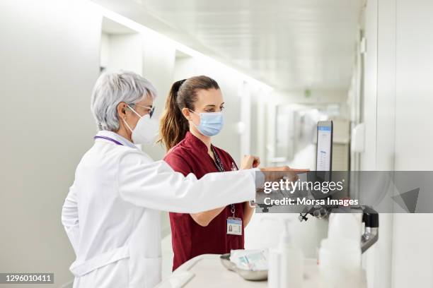 doctor pointing at laptop by nurse in hospital - nurse mask - fotografias e filmes do acervo