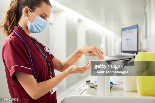 female nurse using hand sanitizer in hospital corridor - handdesinfectiemiddel stockfoto's en -beelden
