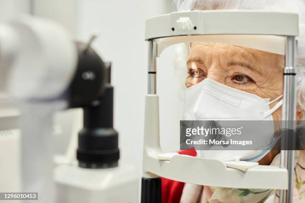 aged woman looking through optometry in hospital - eye test equipment imagens e fotografias de stock