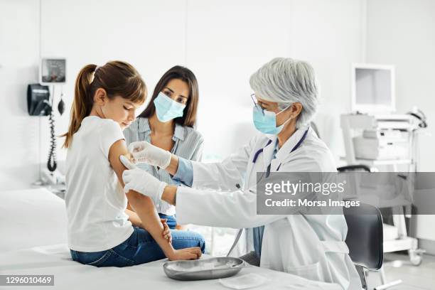 girl receiving covid-19 shot and looking at her arm. - child coronavirus sick stock pictures, royalty-free photos & images