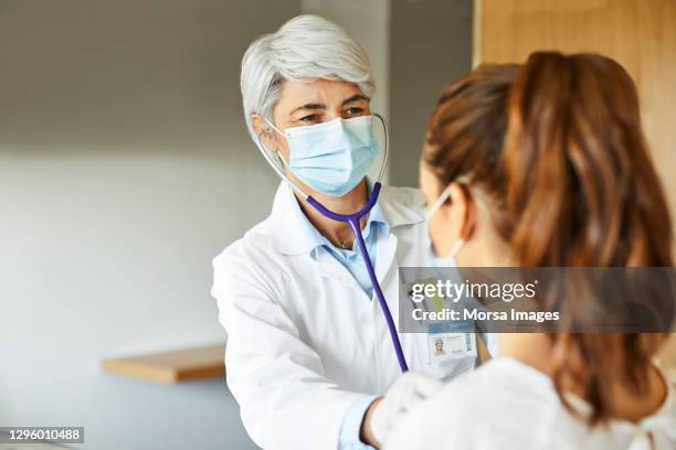 doctor examining female through stethoscope in icu - atemmaske stock-fotos und bilder