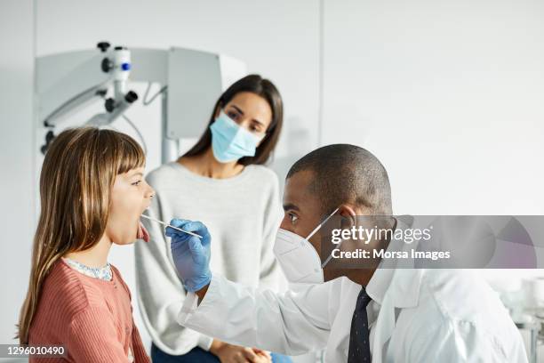 doctor taking swab test sample of girl in clinic - funny face mask stock-fotos und bilder