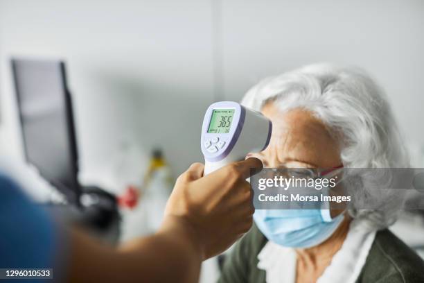 nurse examining patient during covid-19 in clinic - misurare la temperatura foto e immagini stock