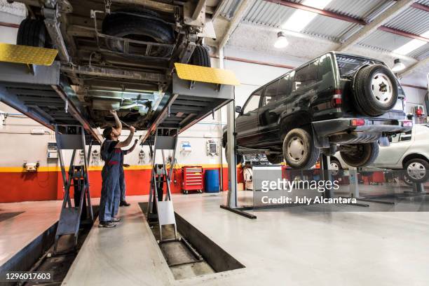 autolift. de monteur controleert de onderkant van een industriële auto, zijn chassis en assen op een hijsbank. - auto garage stockfoto's en -beelden