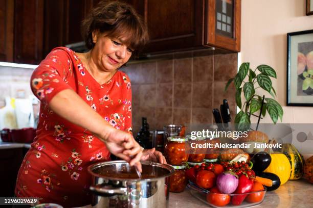 a mature woman stirring a dish in a pot - jars kitchen stock pictures, royalty-free photos & images