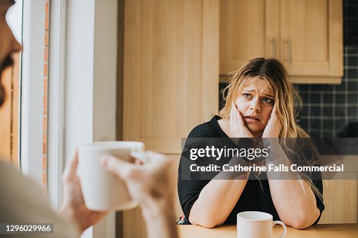 Worried woman sits at a kitchen table holding her head in her hands Worried woman sits at a kitchen table holding her head in her hands