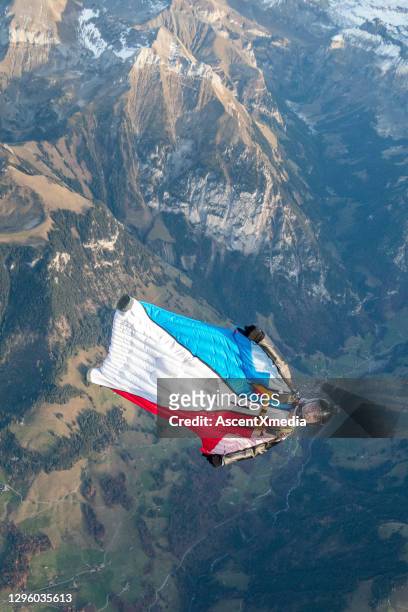 wing suit flier glides upside down over swiss alps - wing suit stock pictures, royalty-free photos & images