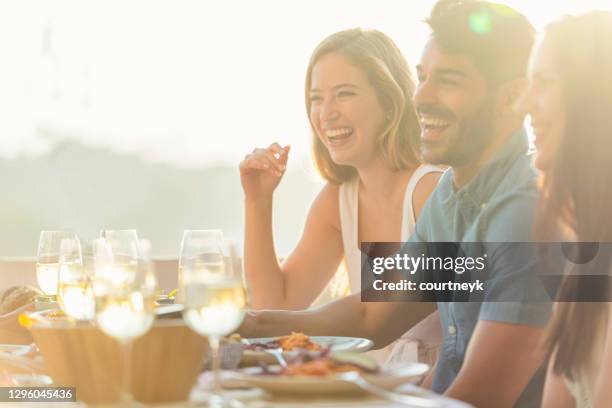 group of friends eating a meal. they are drinking white wine and eating a meal and having fun. - patio restaurant stock pictures, royalty-free photos & images