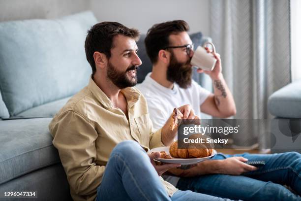 two roommates sitting on floor in living room, having snack. - drinking buddies filme imagens e fotografias de stock