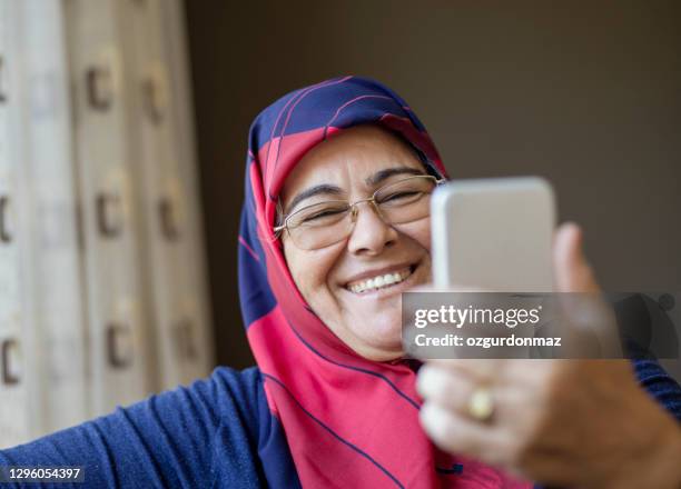 hogere moslimvrouw die een hoofddoek draagt die een selfie, binnen neemt - headscarf home stockfoto's en -beelden